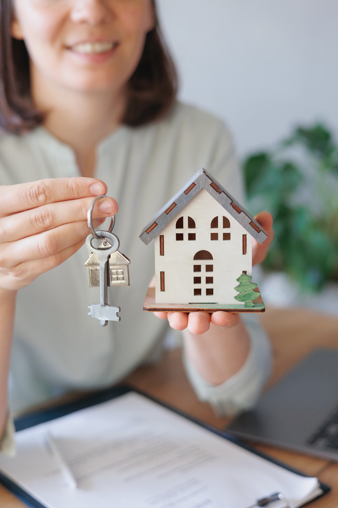 European woman realtor or mortgage agent consultant holds a miniature model of a house and keys